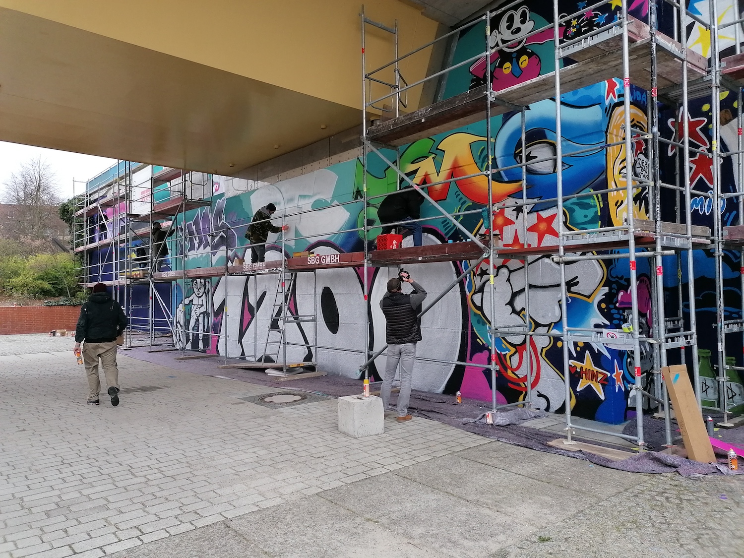 Wand mit Gerüst, auf dem Graffiti-Künstler stehen und sprühen