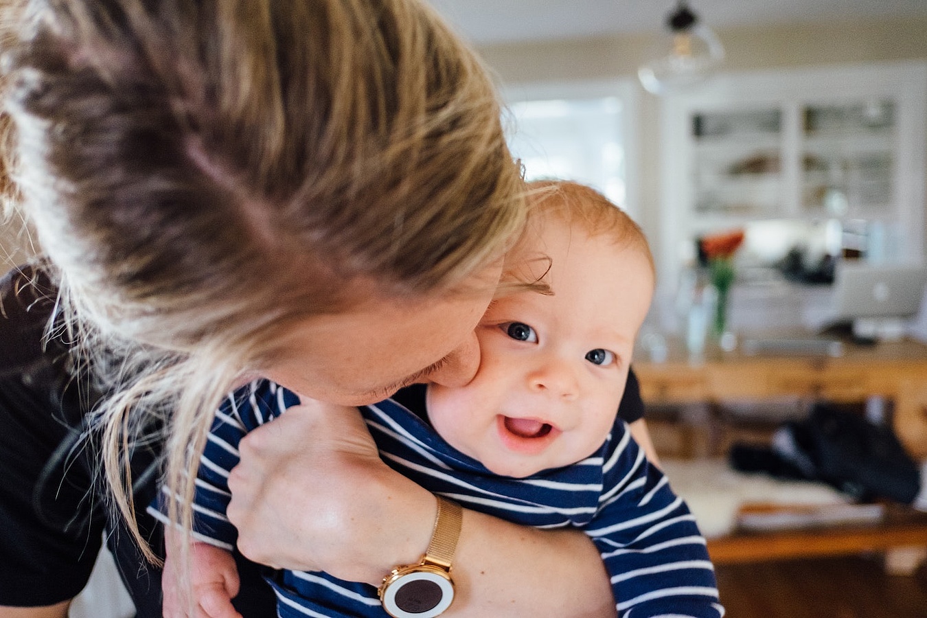 Frau mit blonden Haaren hält Baby auf dem Arm, das in die Kamera schaut