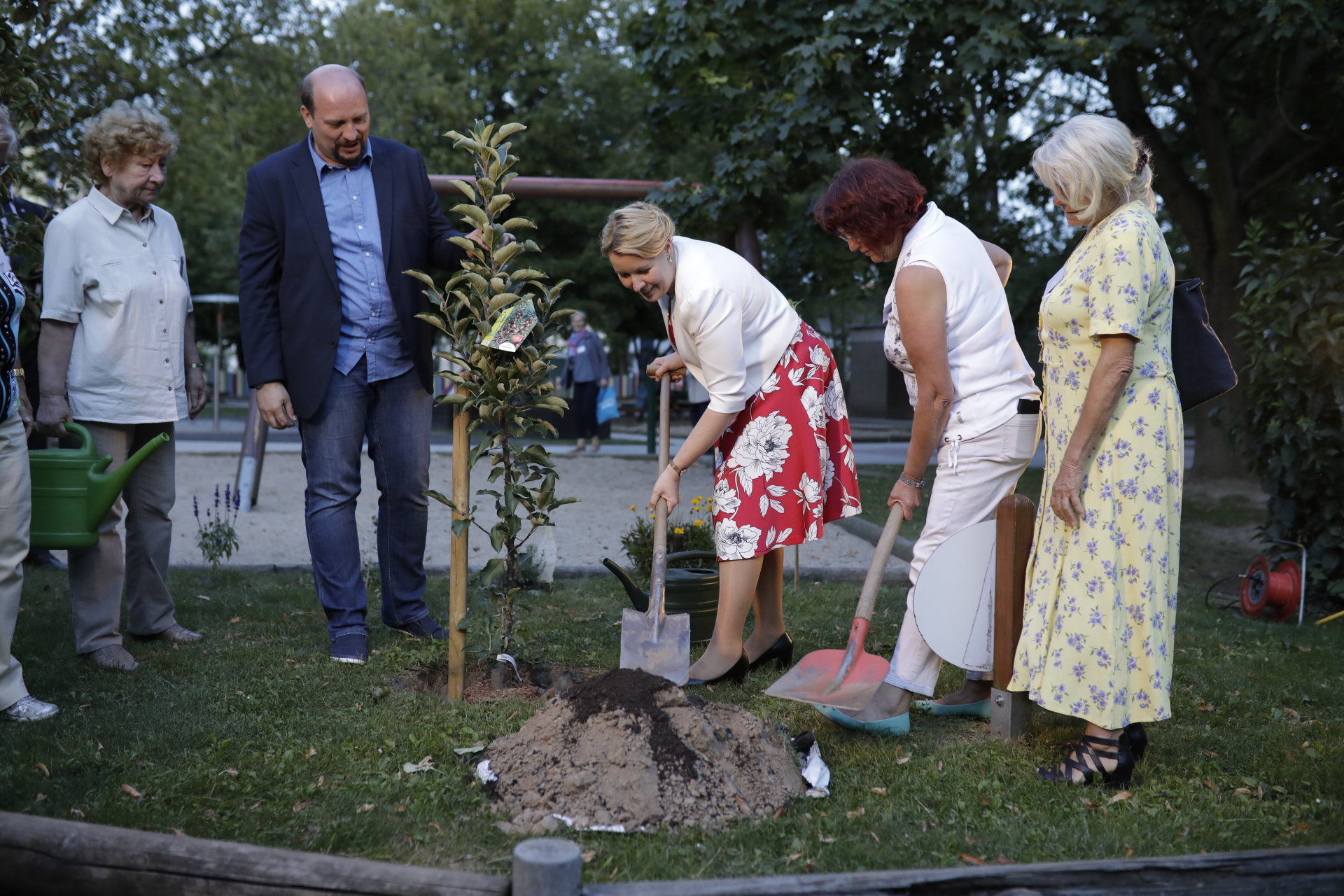 Bundesfamilienministerin Dr. Franziska Giffey und zwei weitere Frauen heben mit Spaten ein Loch in der Erde aus, um einen jungen Baum zu pflanzen. Daneben stehen zwei Männer und schauen zu. 